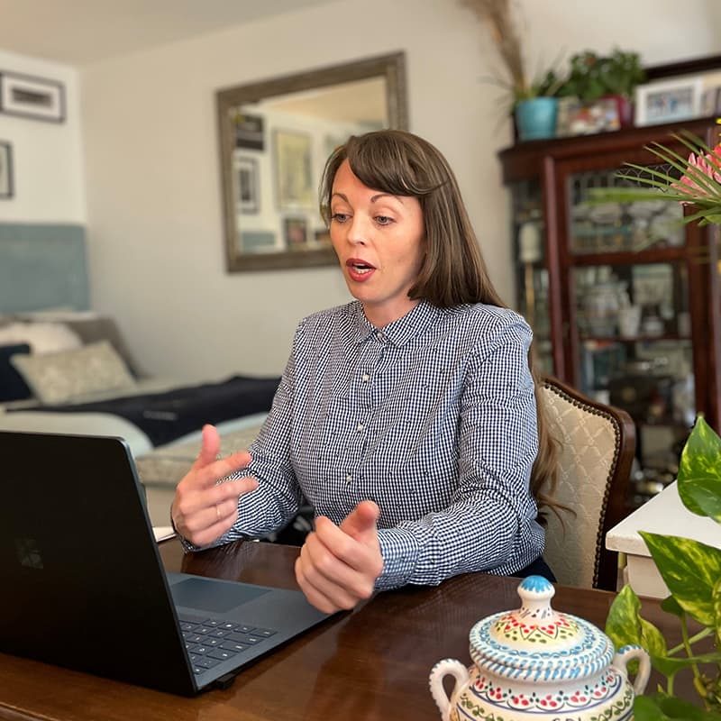 A woman at home looking at a laptop and speaking on a zoom call
