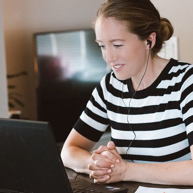 A woman wearing a black and white striped shirt watching a video on a laptop computer
