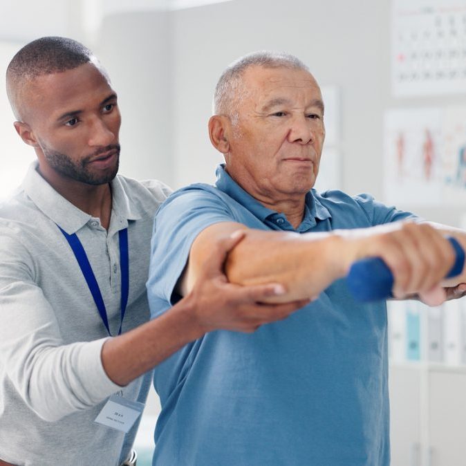An older man lifting weights with a young male physiotherapist.