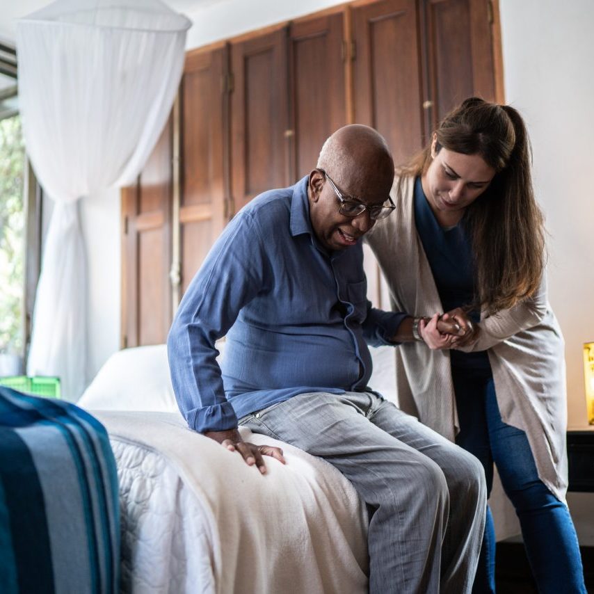 Home caregiver helping a senior man standing up at home