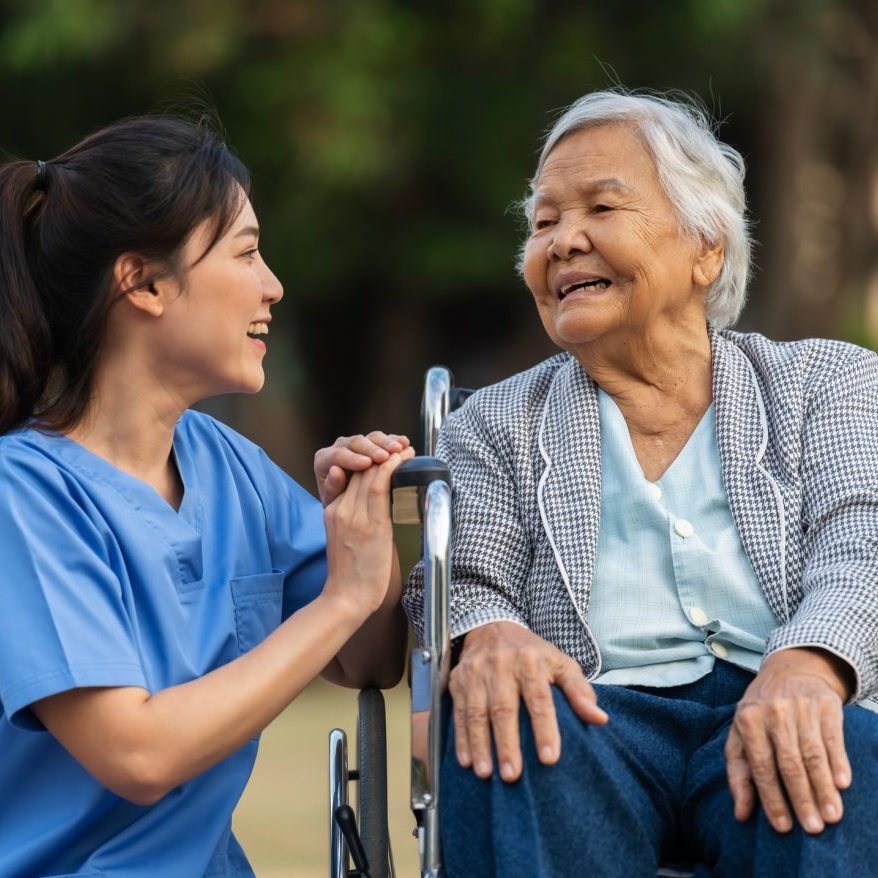 happy nurse take care and talking with senior woman patient in wheelchair at the park, friendly caregiver